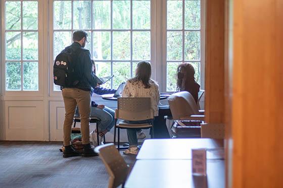 Students sit at a table and work on laptops